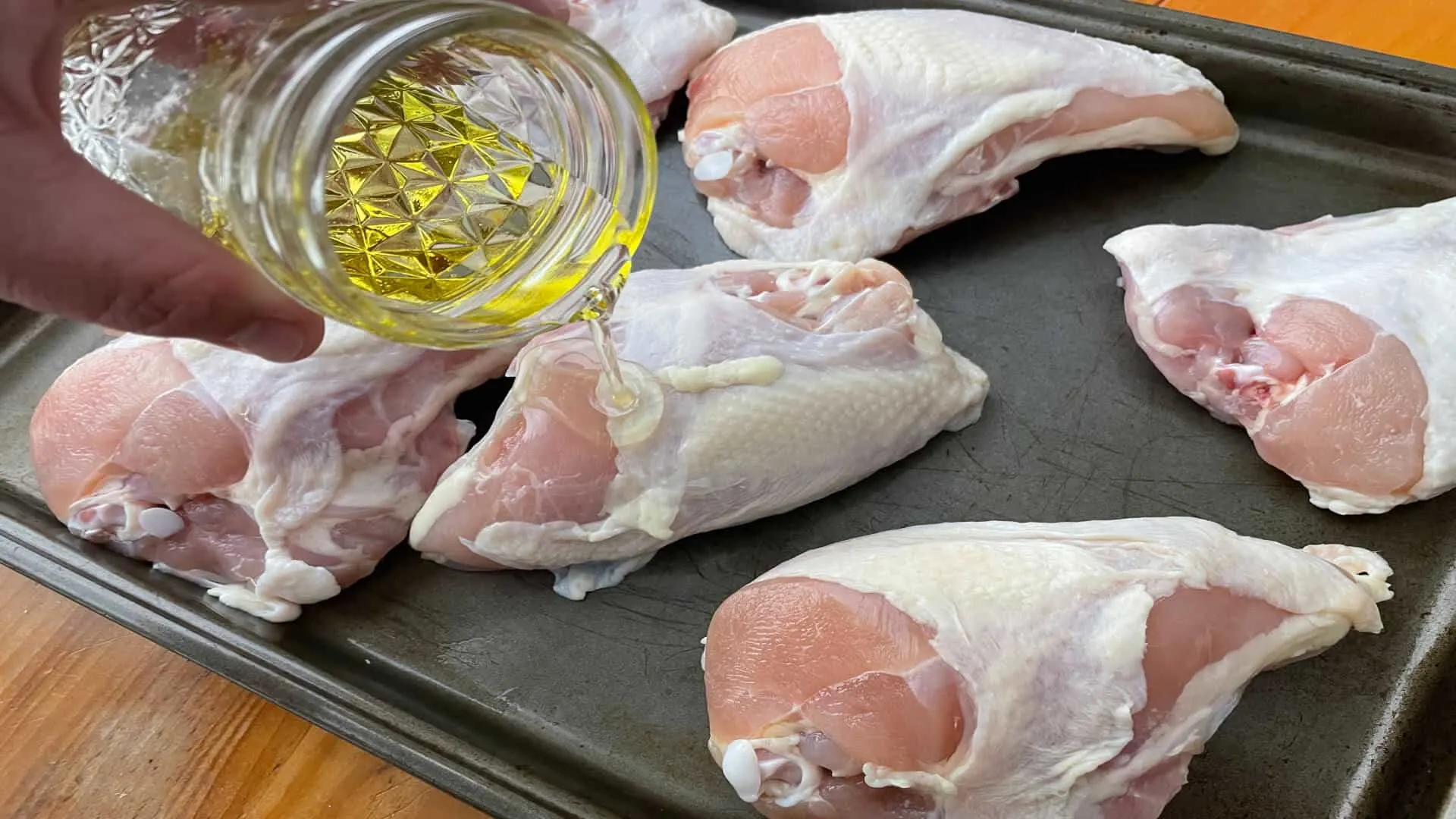 Pouring Olive oil on whole split chicken breast to coat it before adding the Cajun seasoning.