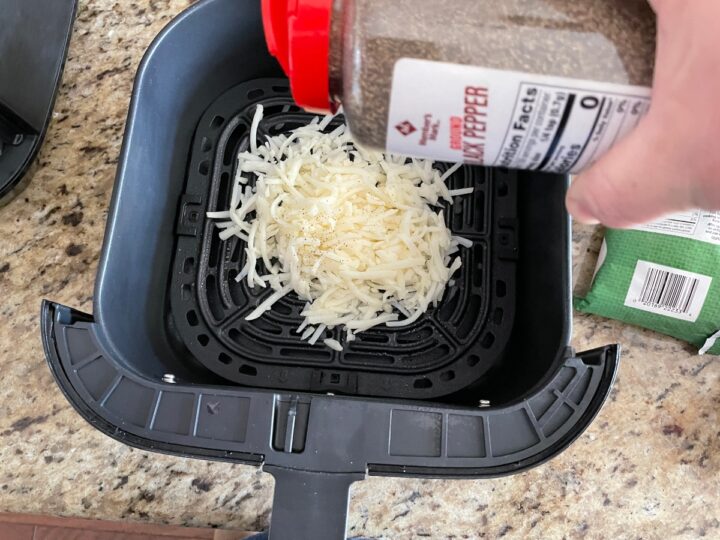 adding black pepper to shredded hash browns before cooking in the air fryer.