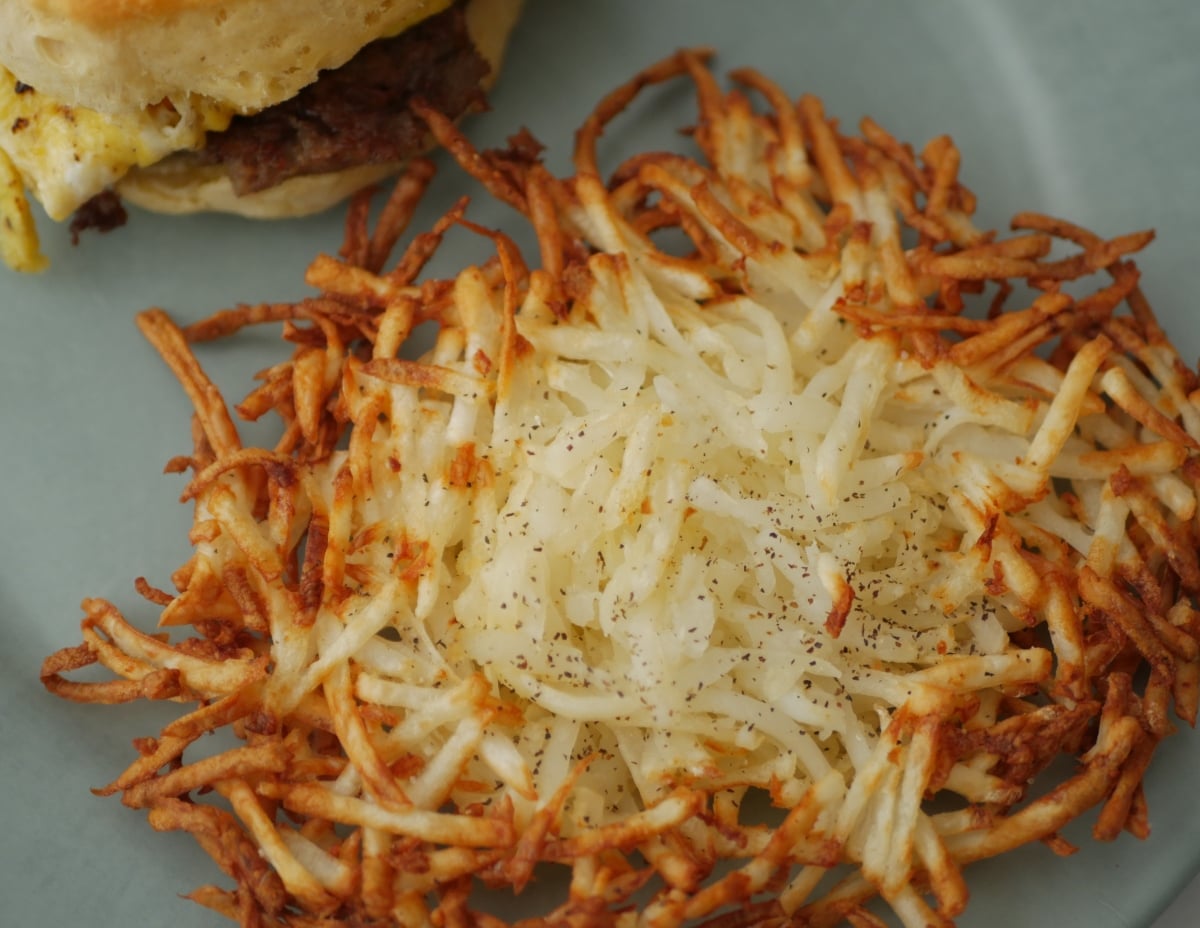 closeup picture of shredded hash browns cooked in the air fryer sitting on a plate with a breakfast sandwich.