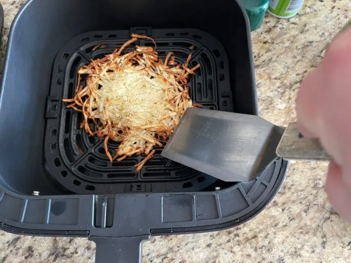 Flipping shredded hash browns half way through cooking in the air fryer.