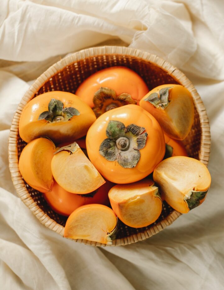Asian Persimmons in a basket with some cut open taken by Photo by Any Lane.