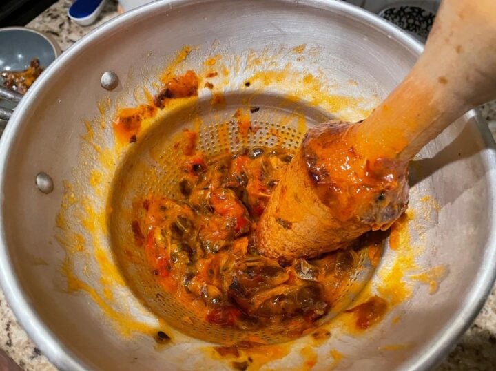 Using a conical sieve (Chinois) and pestel to remove seeds and skin from American Persimmons.