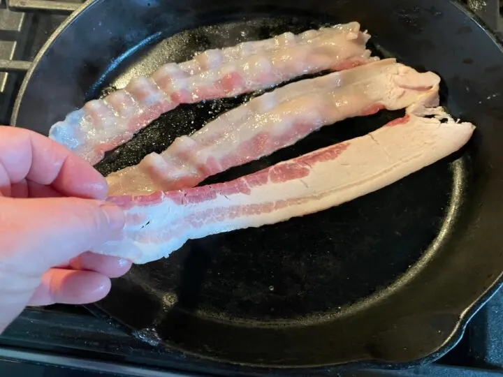 bacon frying in a cast iron pan.