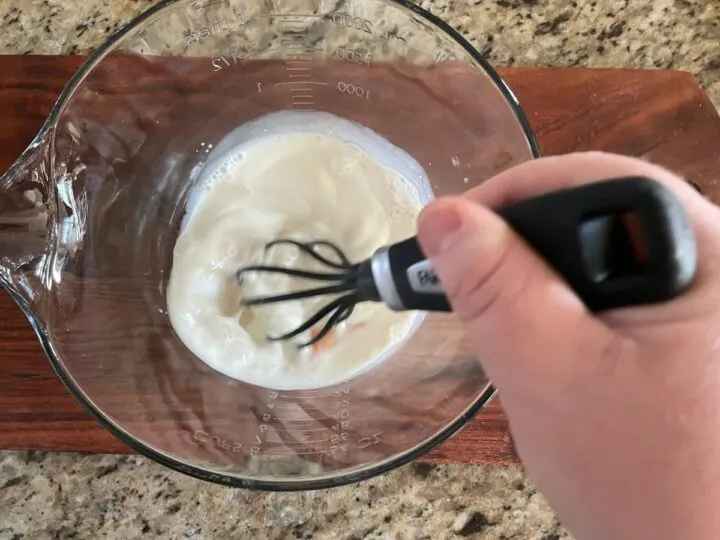 mixing egg and milk together in a mixing bowl to make pancakes.