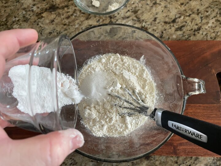 adding baking powder to a mixing bowl for a recipe to make pancakes.