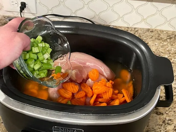 adding celery to a crock pot to make crock pot chicken noodle soup.
