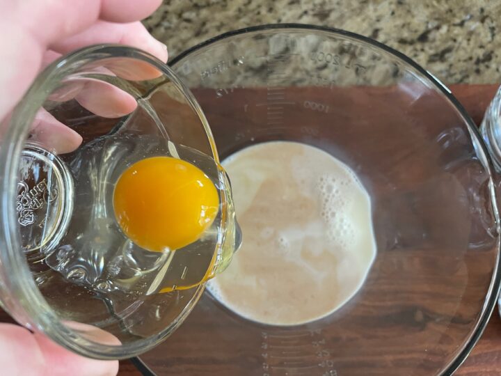 adding a large egg to milk in a mixing bowl in order to make pancakes.
