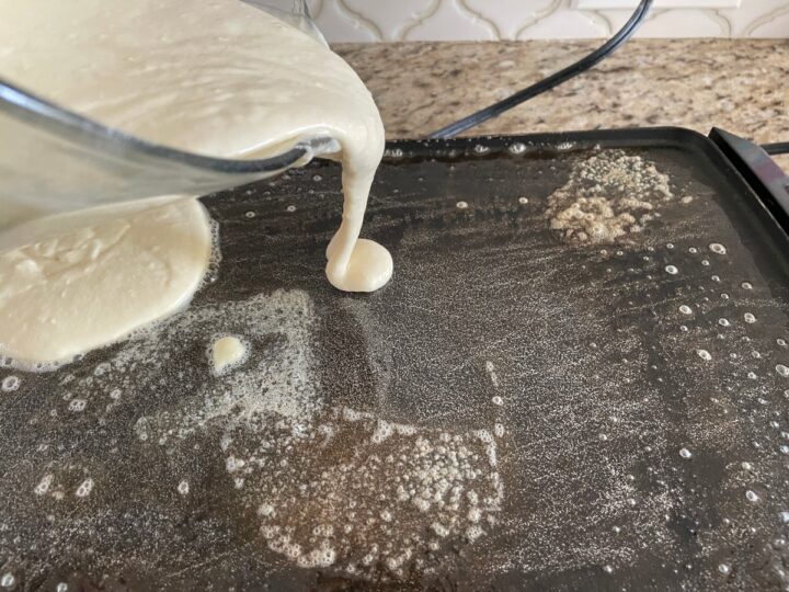 pouring pancakes batter onto a griddled that has melted butter on it.