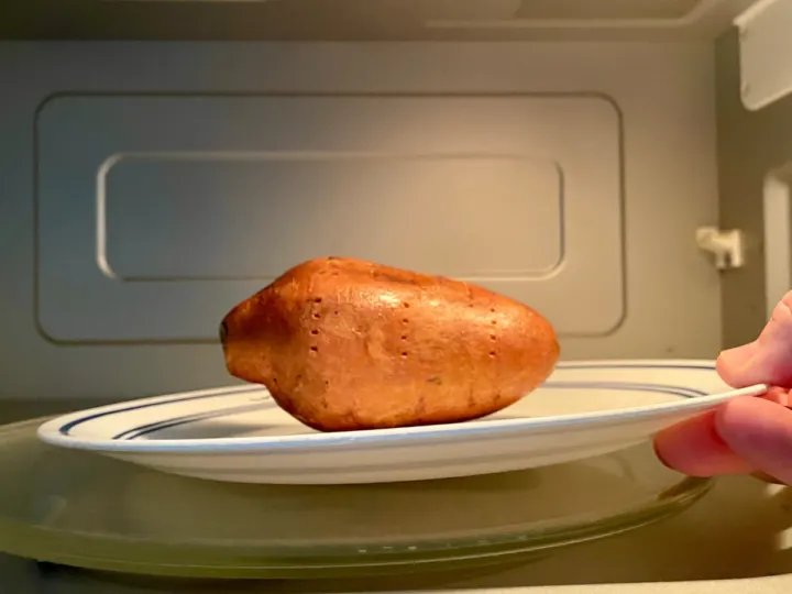 Putting sweet potato in the microwave on a microwave safe plate.