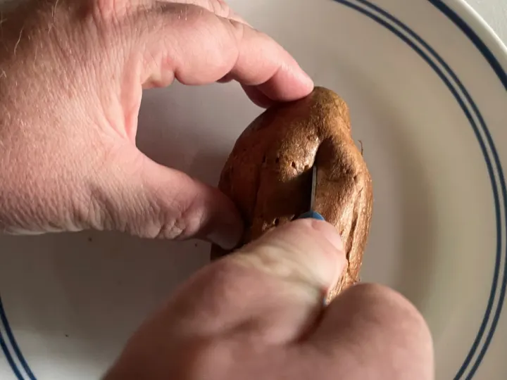 Using a paring knife to cut open the baked sweet potato.