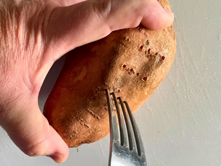 using a fork to puncture holes in a sweet potato.