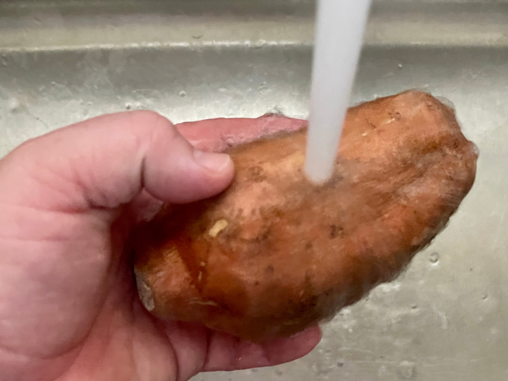 washing and scrubbing a sweet potato before cooking it.