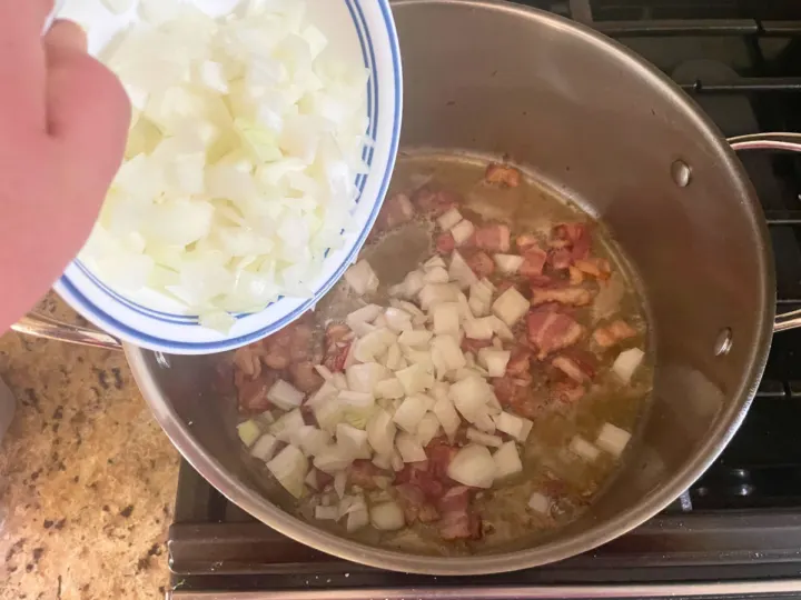 Adding onions to rendered bacon in a stock pot to sweat the onions down.