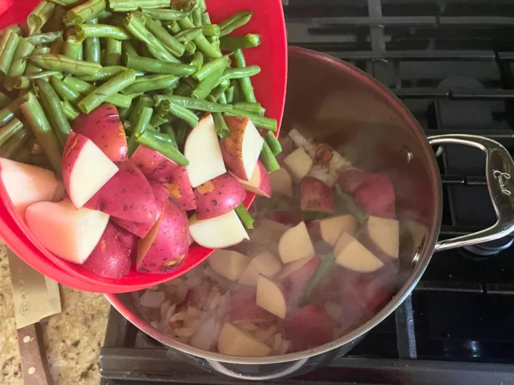 Adding potatoes and green beans to stock pot.
