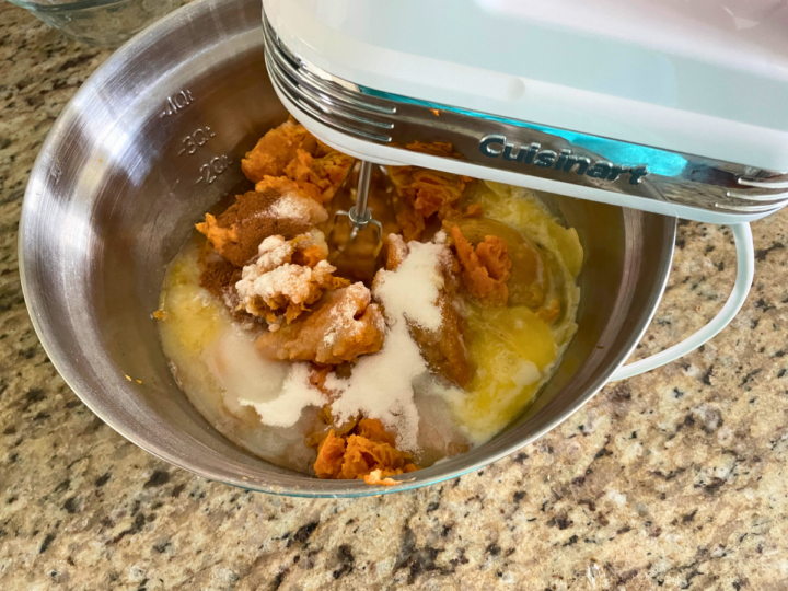 Using a hand mixer to mix all the ingredients together to create the base layer for Sweet Potato Casserole. 