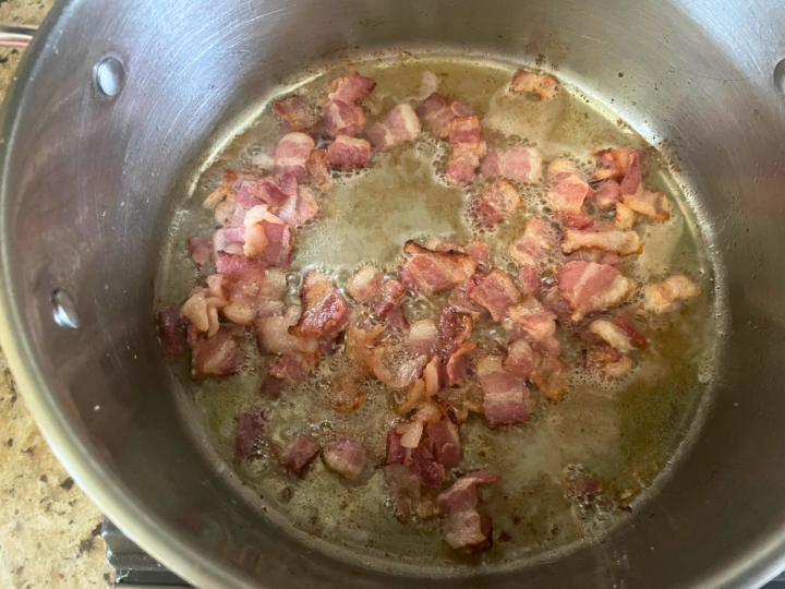 Rendering out fat from bacon by cooking it in a stock pot.