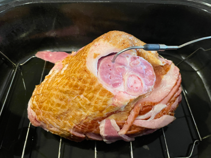 This image shows a remote meat thermometer placed in the center of a smoked ham that is about to be reheated in order to be served.