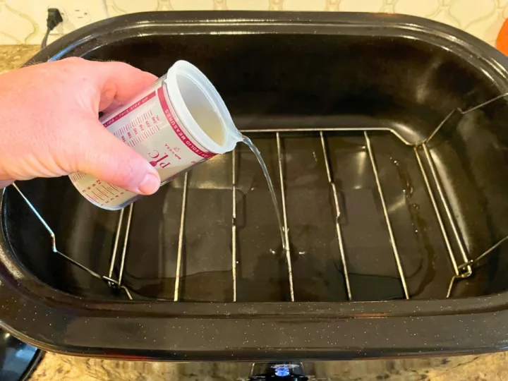 This image is a person adding chicken stock to a roaster oven in order to reheat a smoked ham.