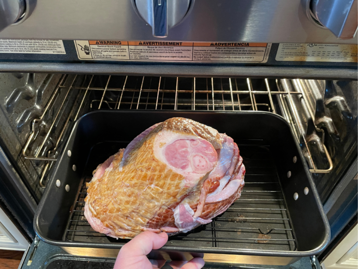 This image shows someone putting a precooked ham in the oven in order to show how to reheat a smoked ham.