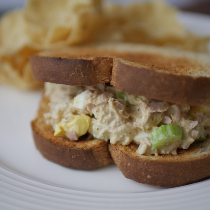 This image is a completed recipe showing southern tuna salad with egg made into a sandwich with chips on the plate.