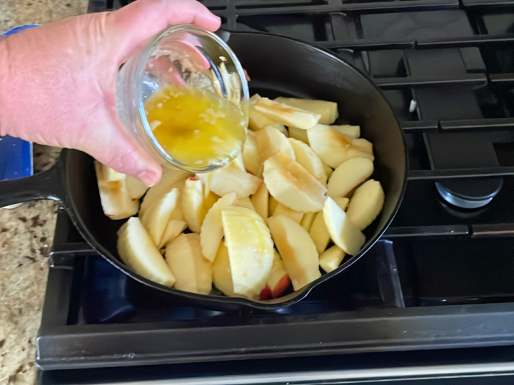 This is a image of pouring melted butter and vanilla extract over top of apples in a cast iron skillet.