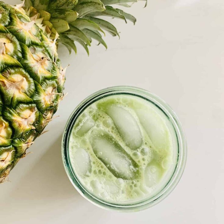 This is a over head shot of a glass of Pineapple matcha iced tea. There is a pineapple sitting to the left of the glass quartering away.