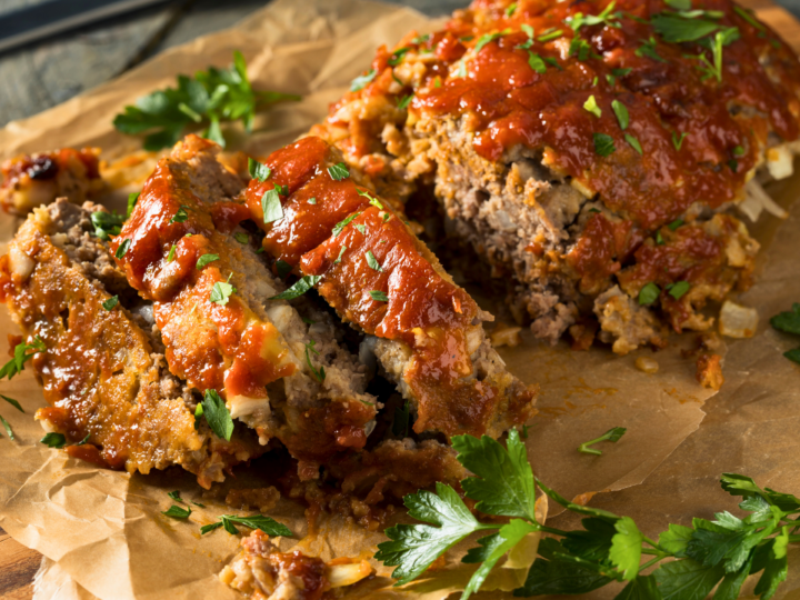 This is a closeup image of meatloaf. Half of the meatloaf is sliced where you can see the texture and the ingredients in it. 