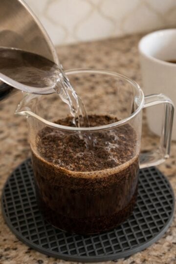 Pouring hot water over coffee grounds in a French press to demonstrate the correct coffee-to-water ratio