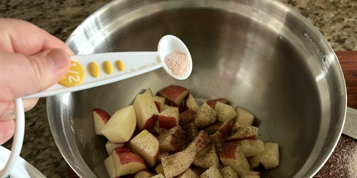 Adding sea salt to diced red potatoes in a mixing bowl before air frying
