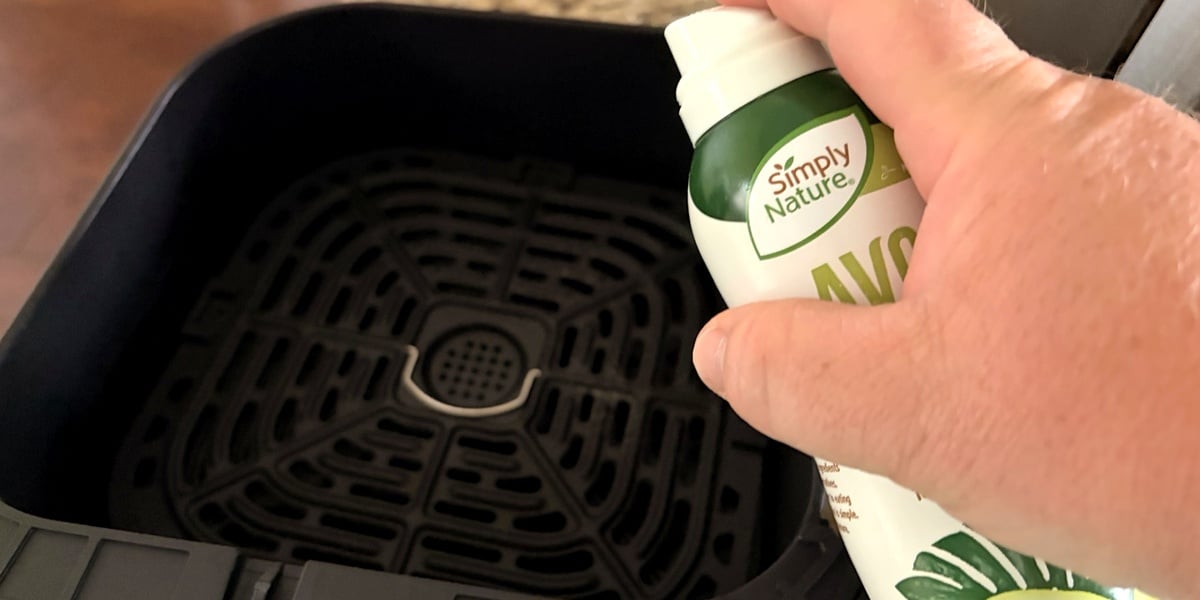 Spraying air fryer basket with olive oil before cooking potatoes