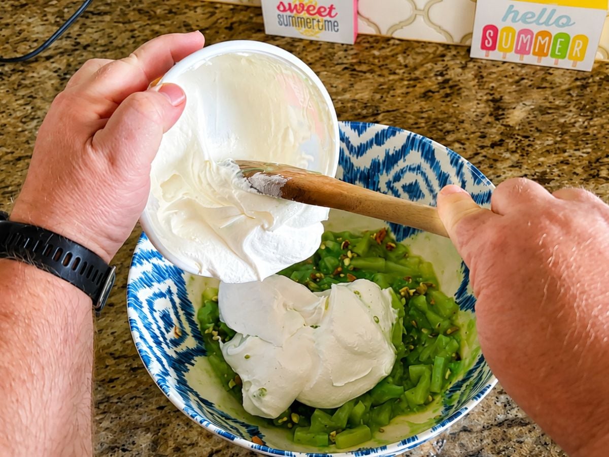 Adding Cool Whip to the pistachio pudding and pineapple mixture while making Watergate Salad.