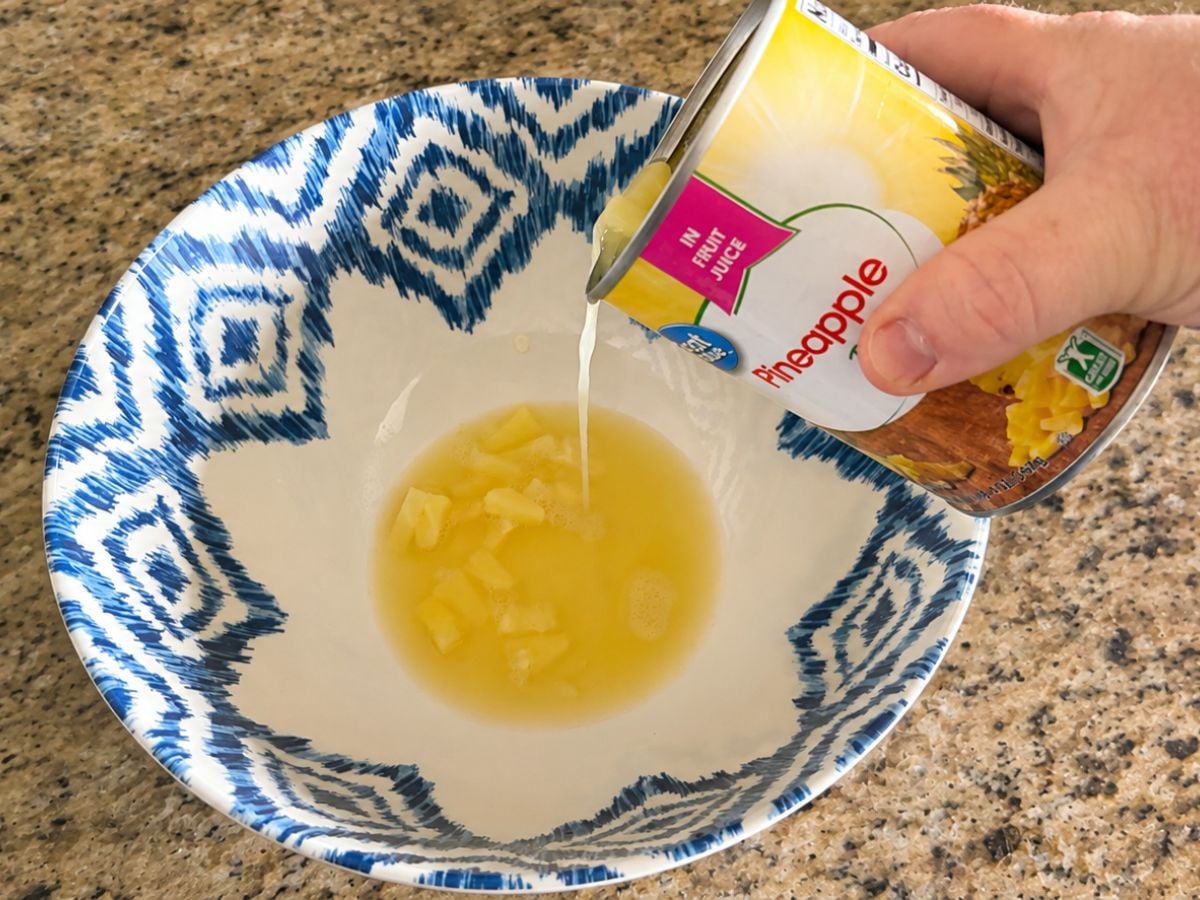 Pouring pineapple with juice into a mixing bowl to make Watergate Salad.