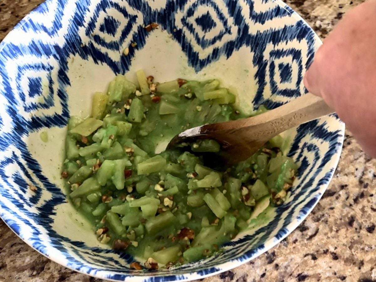 Mixing crushed pineapple, pistachio pudding mix, and pecans together for Watergate Salad.