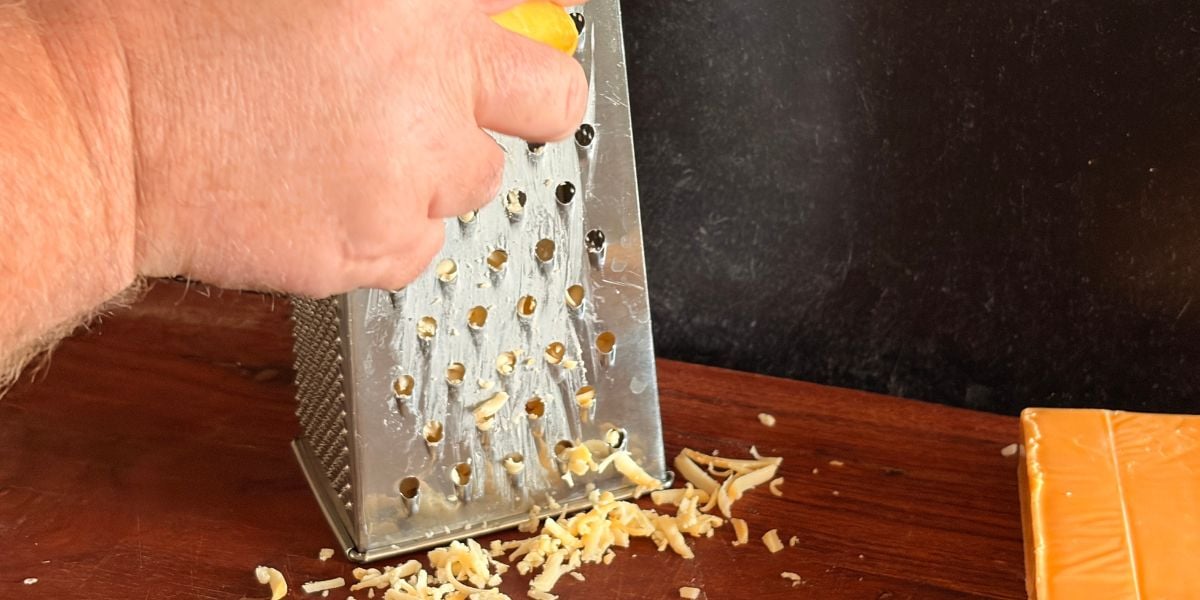 Fresh smoked Gouda being grated on a box grater.